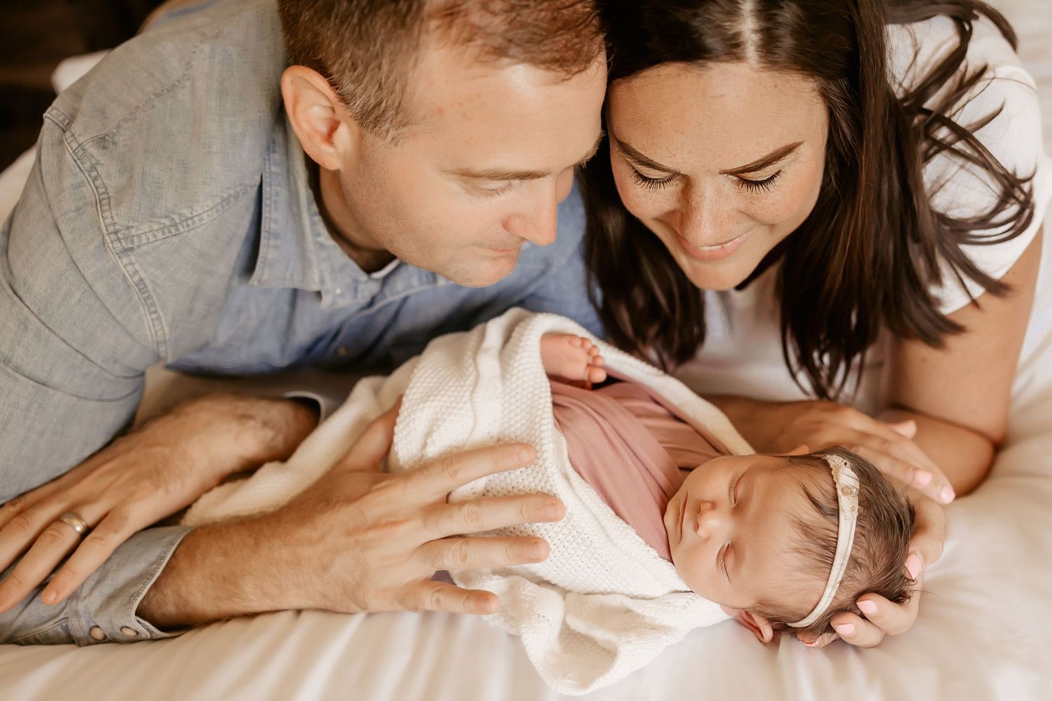 A Honolulu Newborn photographer captures parents looking down at their newborn baby girl while she sleeps.