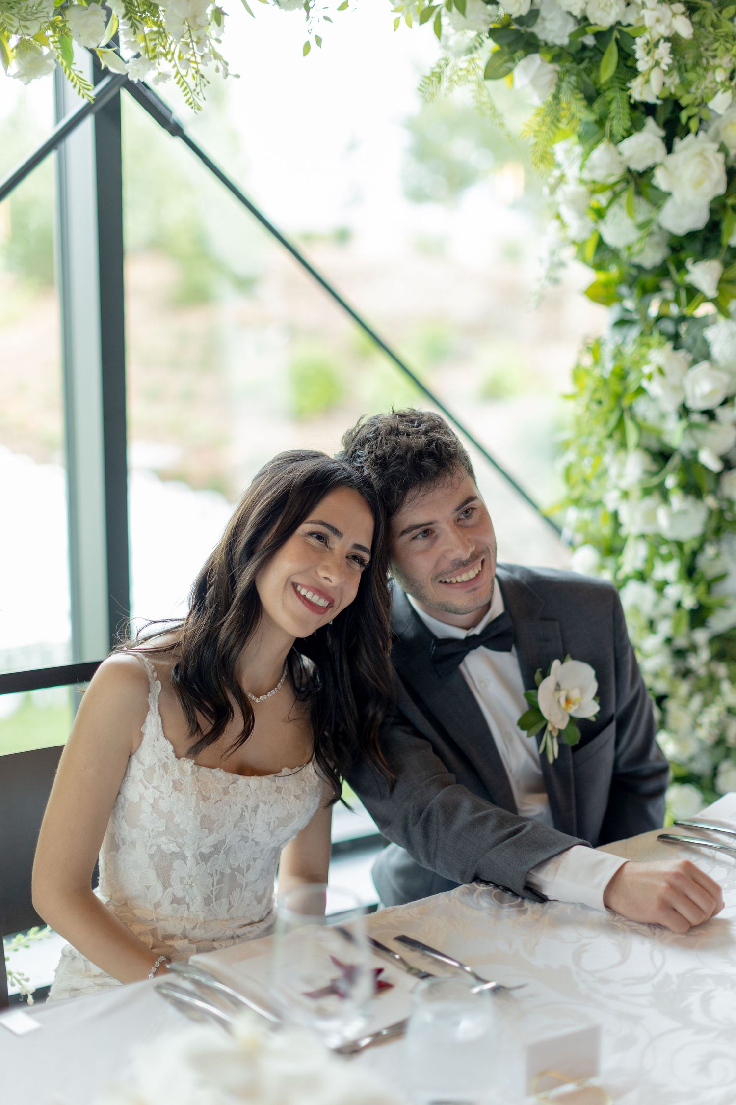Wedding couple signs documents under floral arch with white roses.