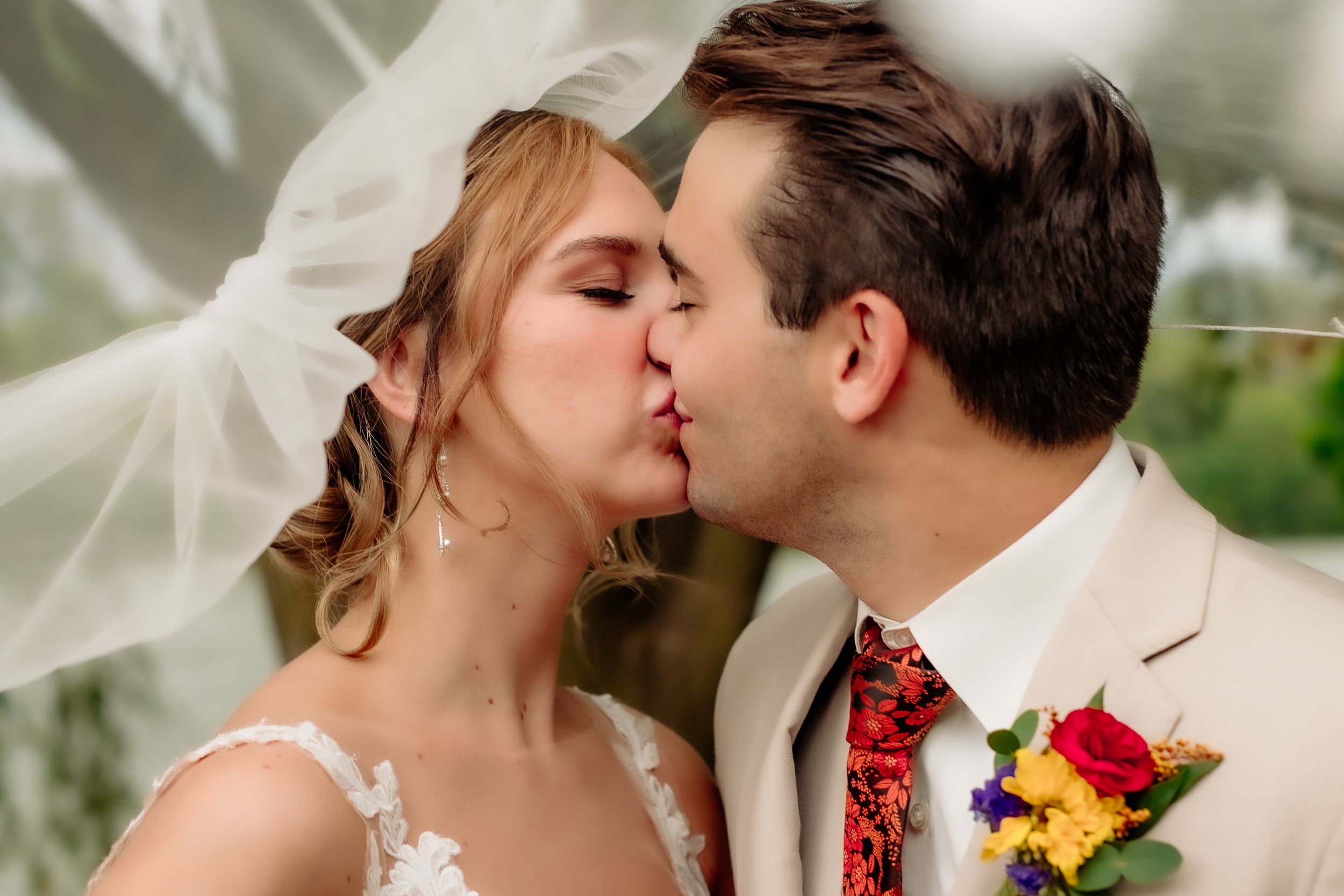 A Buffalo N.Y. Bride and Groom share a kiss under a flowing white veil during wedding portraits at Delaware Park at Hoyt Lake in Buffalo N.Y