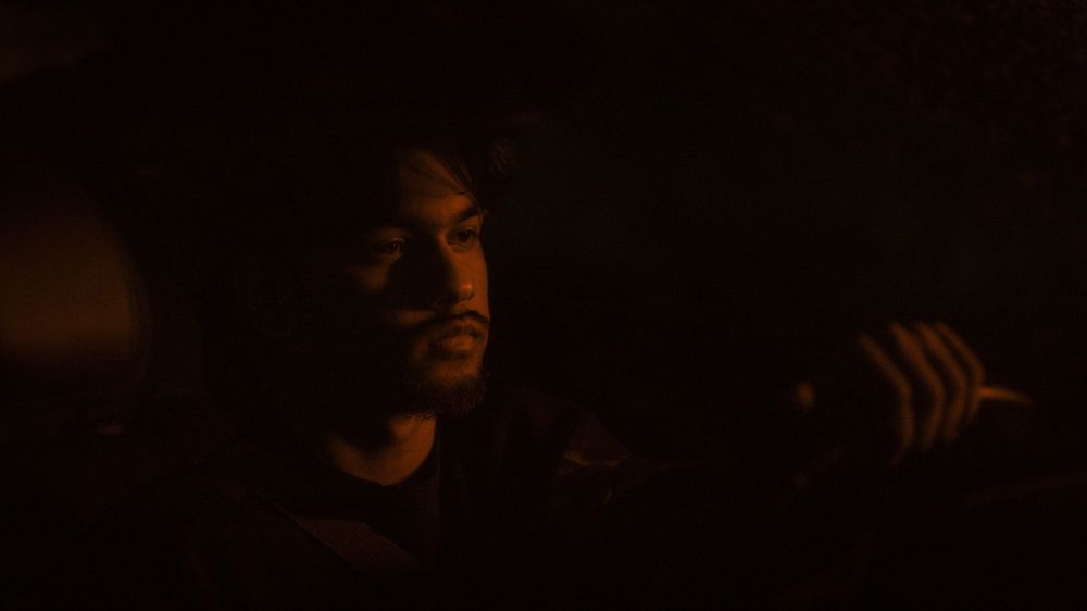 A person is illuminated by warm orange light in a dark moody environment.