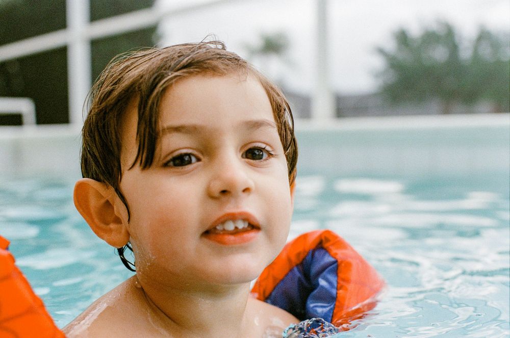 Someone wearing orange flotation devices enjoys swimming in a bright blue pool.