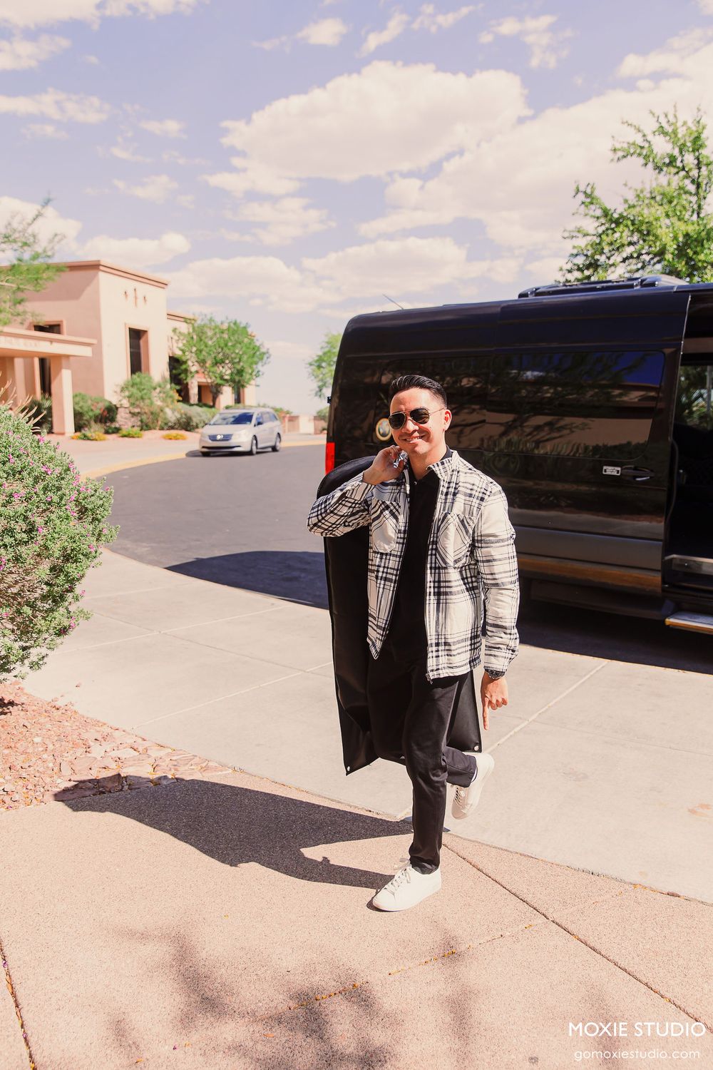 A black stretch limousine parked in a sunny desert driveway with palm trees and stucco buildings in the background.