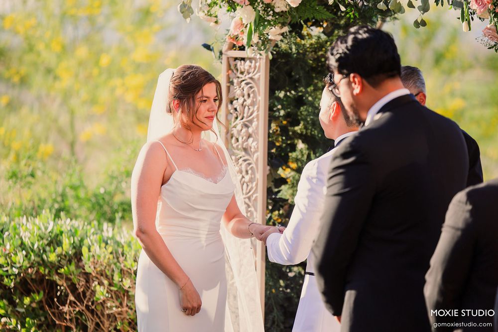 A romantic wedding ceremony takes place under a floral arch with soft yellow foliage in the background.