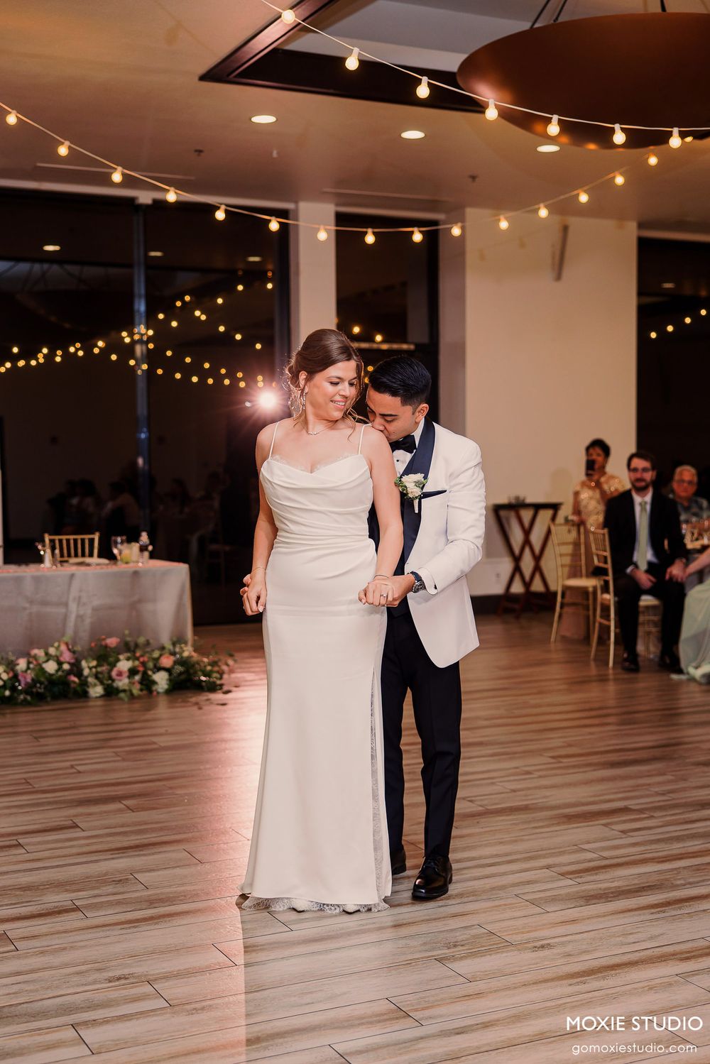 Couple dancing together in an elegant venue with string lights overhead during their first dance.