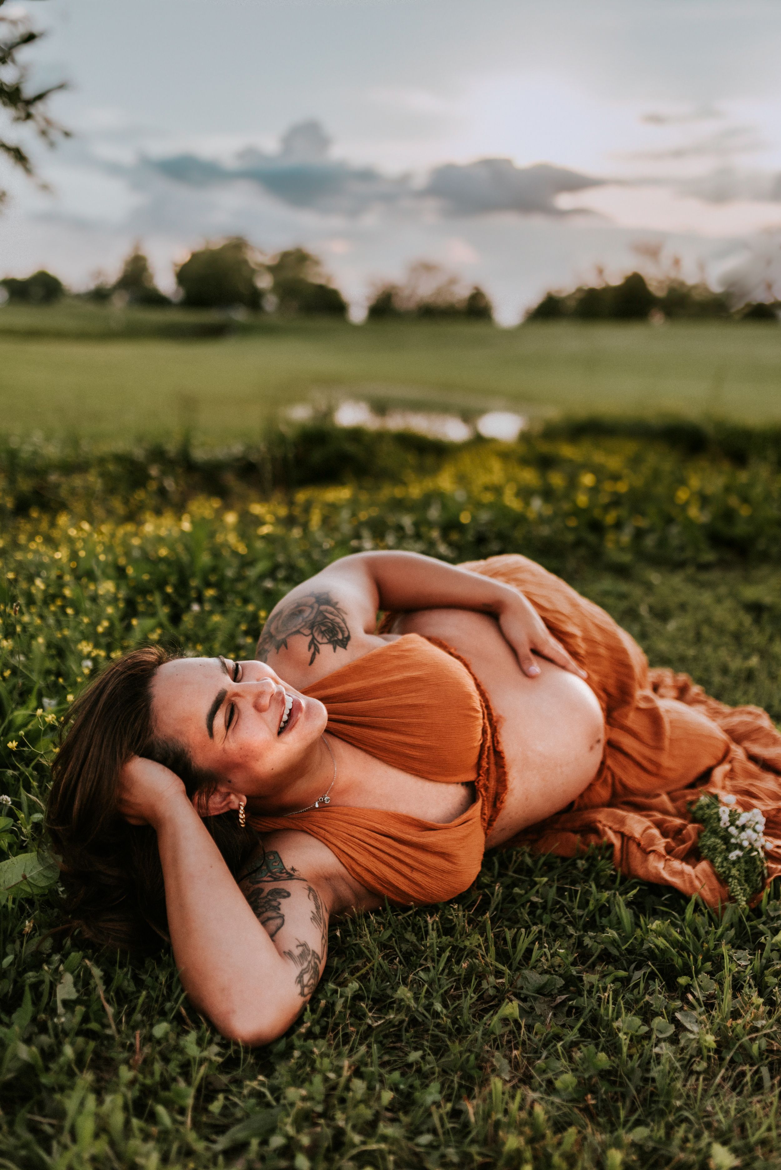 Maternity portrait of an expecting mother laying on her side touching her belly with wild flowers around her in client closet dress in TN