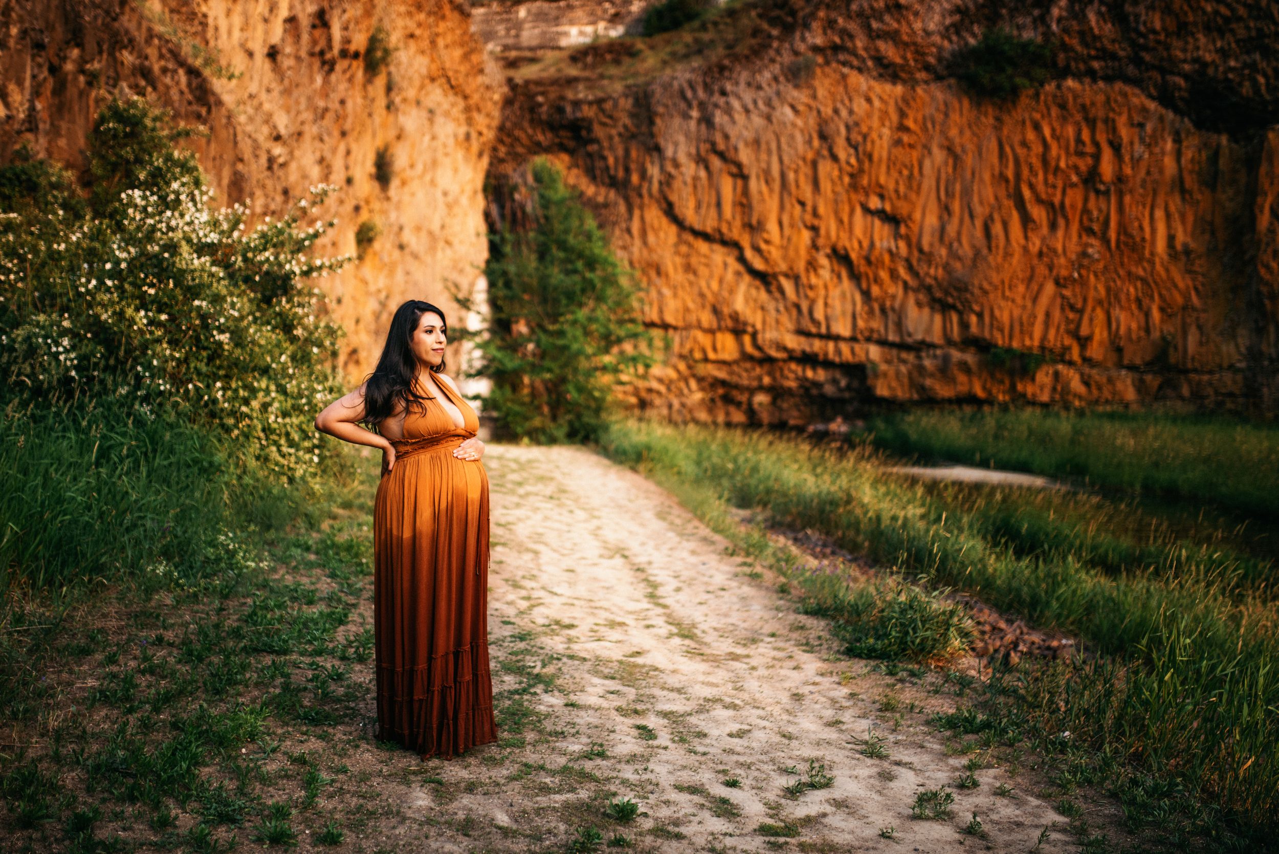 Expecting Mother with hand on her belly standing in front of rock formation in Spokane, Washington.