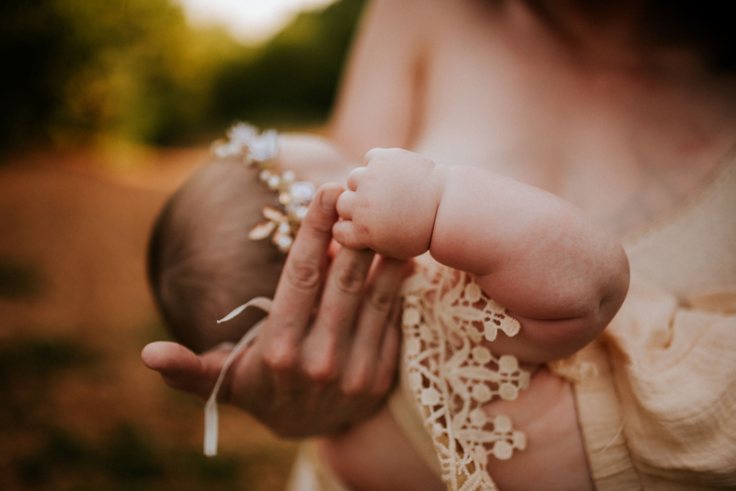 A six month of baby holding her mother's finger as she nurses while wearing a flower crown at Fort Campbell, Tennessee.