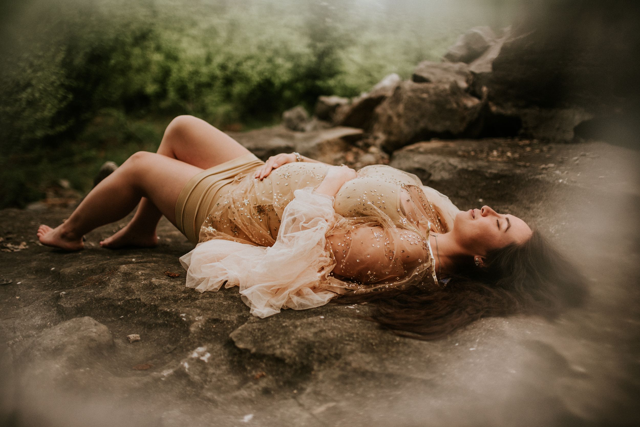 A maternity photo of a mother laying on her back holding her belly in outdoor nature using client closet dress in Fort Campbell, Tennessee.