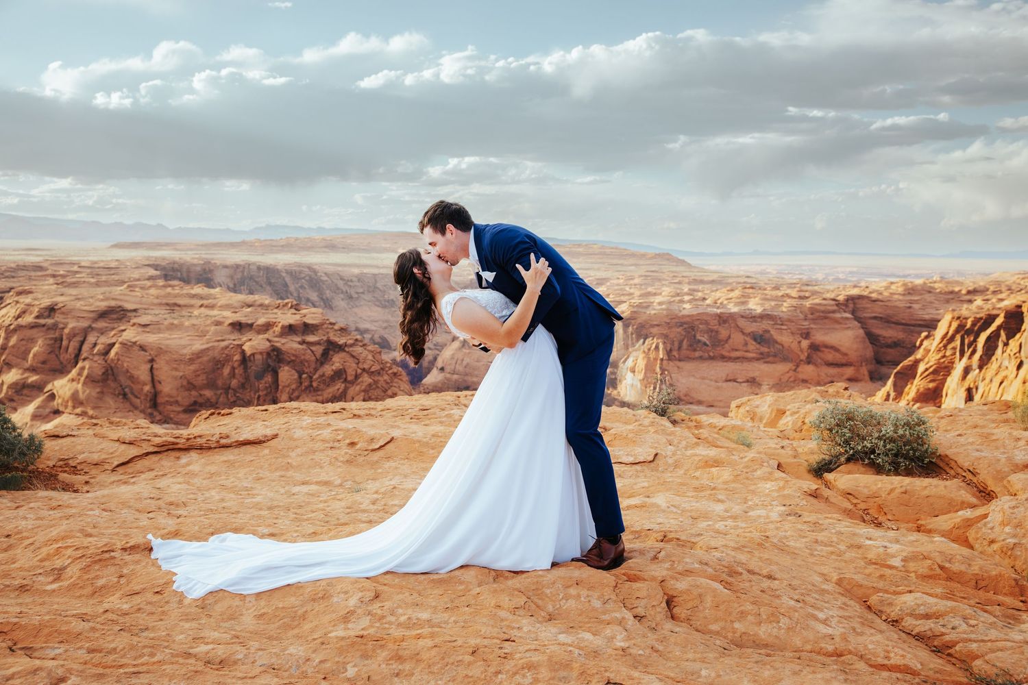 A couple embraces against the dramatic backdrop of red rock canyons and desert cliffs at sunset.