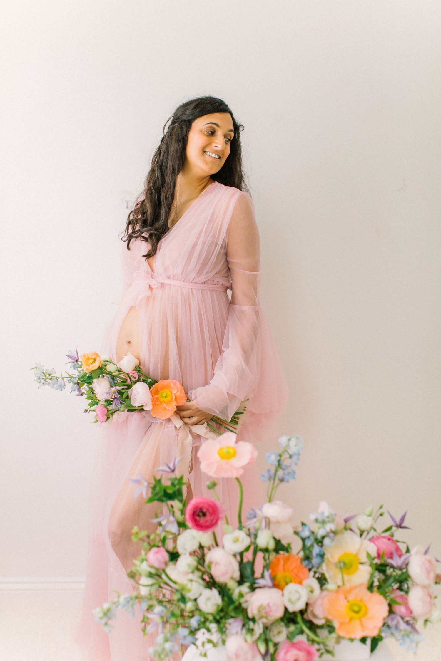 Maternity portrait with pink tulle dress surrounded by colorful spring flowers.