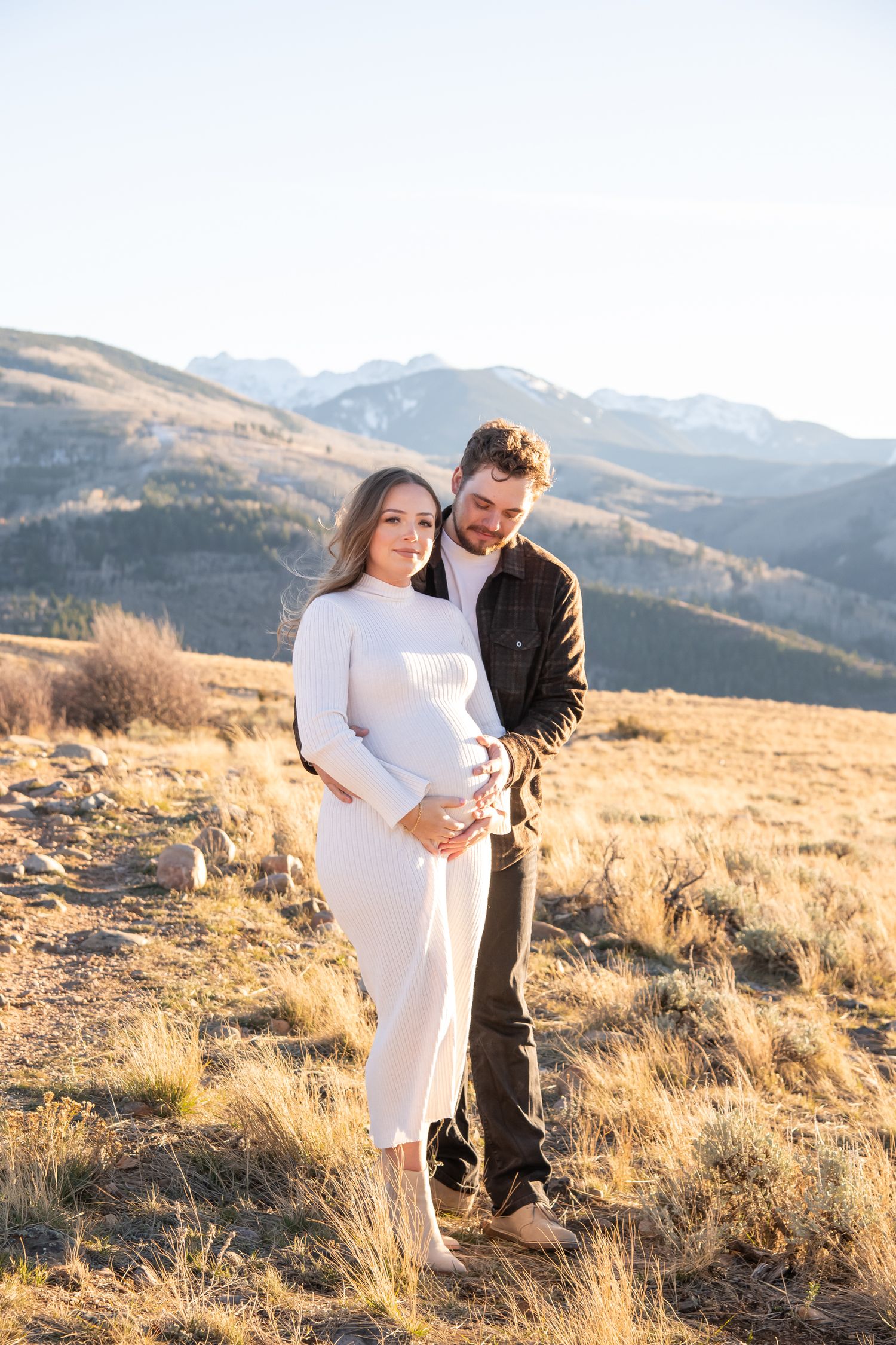 A couple embraces in a romantic mountain setting during golden hour as sunlight illuminates the dry grass landscape near Vail Colorado.