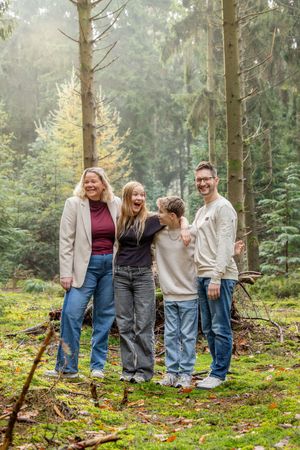 gezin van vier staan in naaldbos met magisch zonlicht achter hen