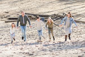 Gezin van vijf rent hand in hand tegen een zand verstuiving omhoog tijdens hun gezinsshoot in het Overijsselse Hellendoorn