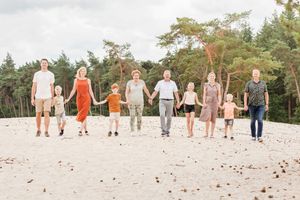 Grote familie lopen naast elkaar, hand in hand tijdens een familiefotoshoot op een zomerse dag