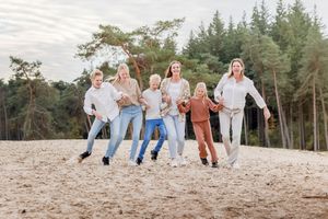 Gezin van zes op een rij, botsen met de heupen tegen elkaar tijdens een gezinsfoto op de Sahara bij Ommen