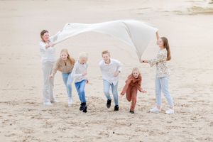 Gezin van zes. Moeder en vrienden houden kleed omhoog waar de kinderen onder door rennen tijdens een fotoshoot op een zandvlakte