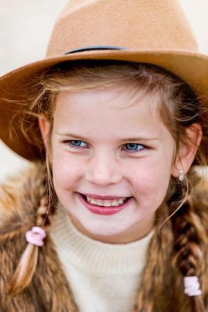 Meisje van 8 jaar met twee vlechtjes en een bruine hoed, lachend en opzij kijkend. Gefotografeerd tijdens een gezinsshoot door Inge Muller