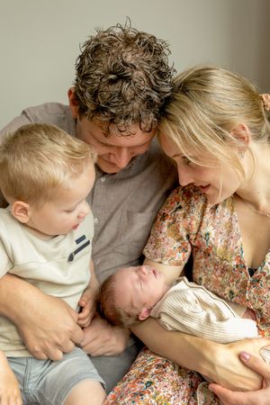 Jong gezin met peuter en baby. Allen kijkend richting een slapende baby op moeders arm tijdens een newbornshoot in Lemelerveld