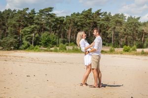 Verliefde stel, zomers gekleed voor hun loveshoot op een zandverstuiving in Overijssel. Staan tegenover elkaar en lachen