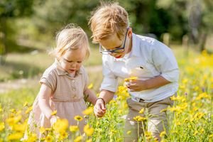 Twee jonge kinderen, broer en zus, staand in een veld met gele bloemen in Haarle. Kijkend naar de bloemetjes. Gemaakt door Inge Muller