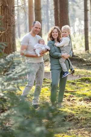 Jong gezin van vier met pasgeboren baby, lopend tussen de naaldbomen op de Lemelerberg