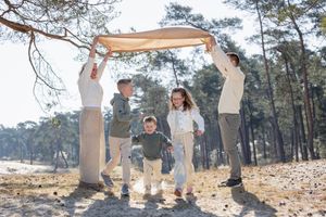 Gezinsfoto waarbij ouders een kleed omhoog houden en de drie kinderen er onderdoor rennen