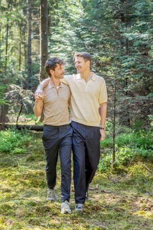 verliefd koppel die in het bos wandeling, terwijl ze elkaar vasthouden over de schouders en lachend naar elkaar