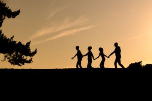 silhouetfoto waarbij gezin van vier zijwaarts hand in hand loopt richting een boom