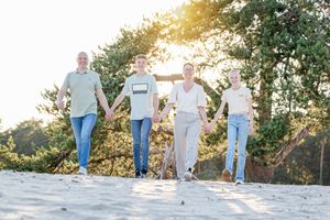 gezin van vier lopen hand in hand met de ondergaande zon achter hen. foto gemaakt door Inge Muller uit Lemelerveld