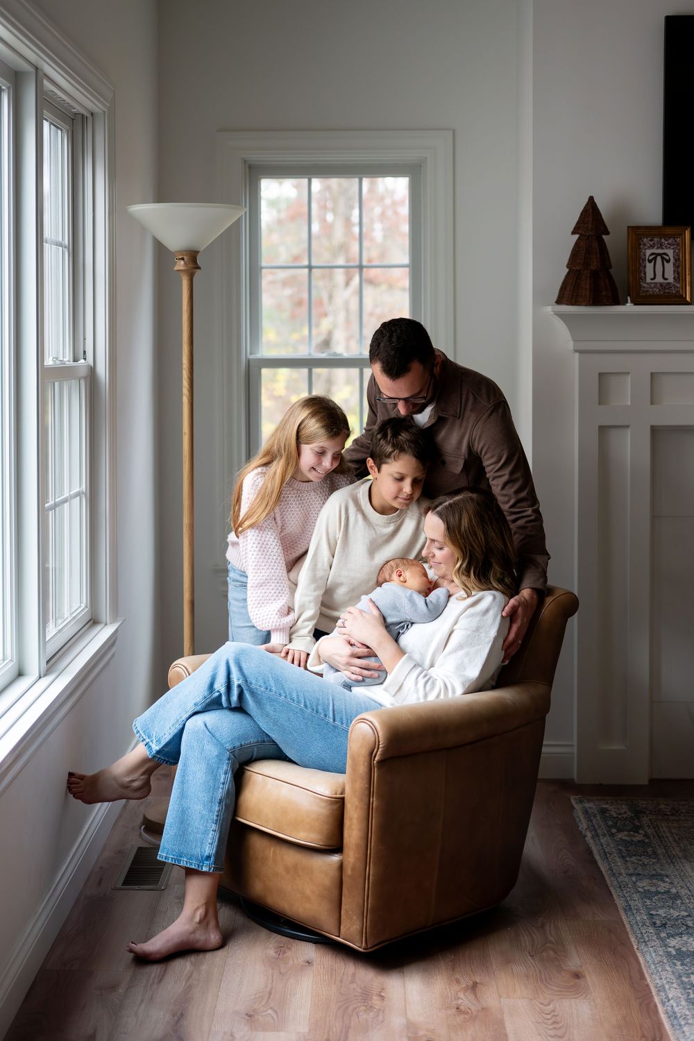 Family of five gathered around newborn baby in leather chair by window.