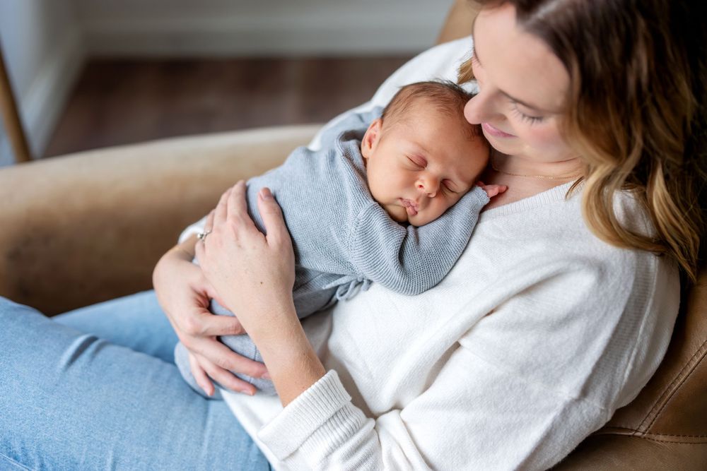 New mother cuddling sleeping newborn baby dressed in blue on chest.