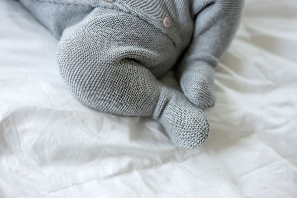 Detail shot of newborn baby feet in gray knit romper on white sheets.