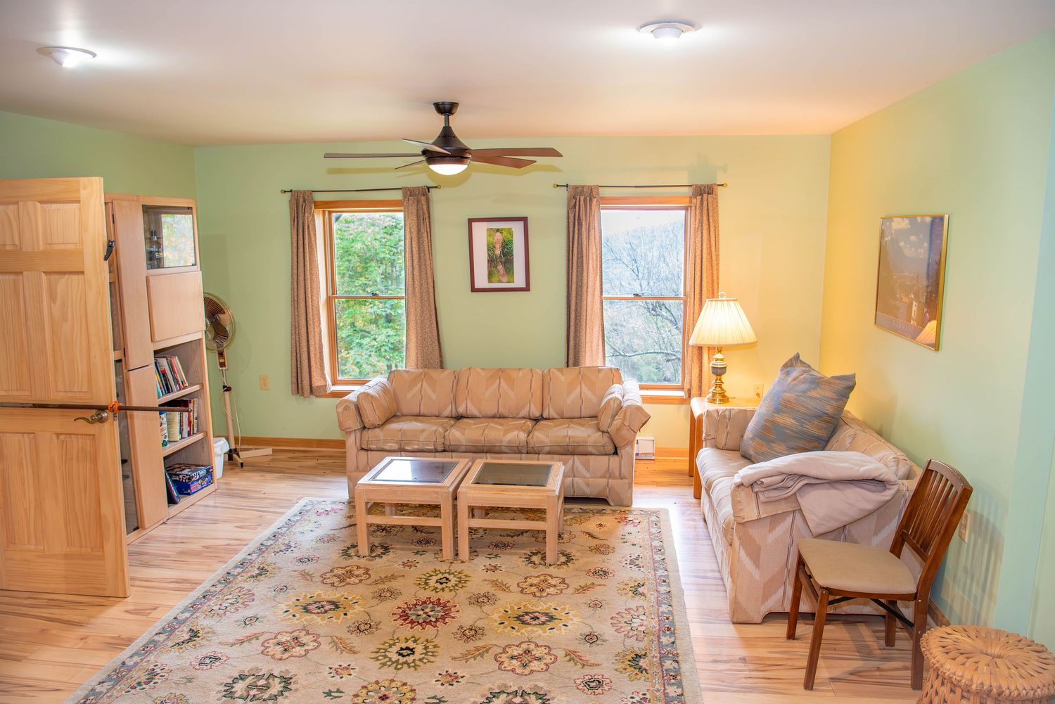 Living room interior with light green walls, ceiling fan, and beige furniture arranged around the space.