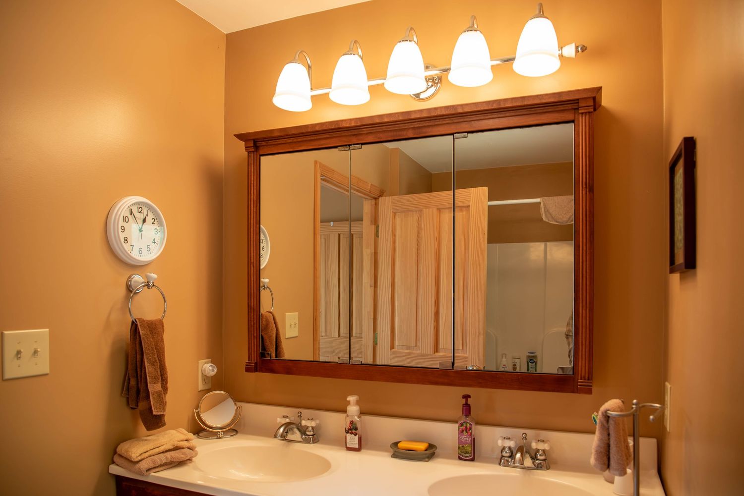 Modern bathroom interior with warm lighting features a large framed mirror and multiple wall sconces mounted above.