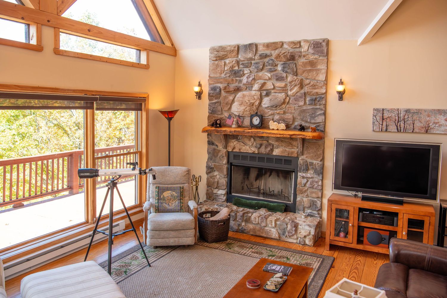 Modern mountain cabin interior featuring stone fireplace, wood beams, and open living space with panoramic windows.