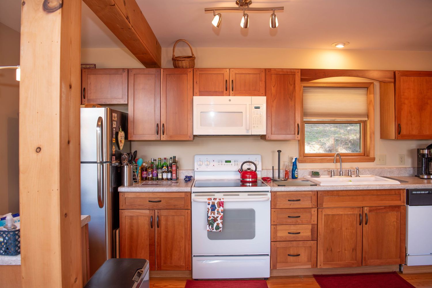 Modern kitchen interior with wooden cabinets, white appliances, and track lighting mounted on the ceiling.
