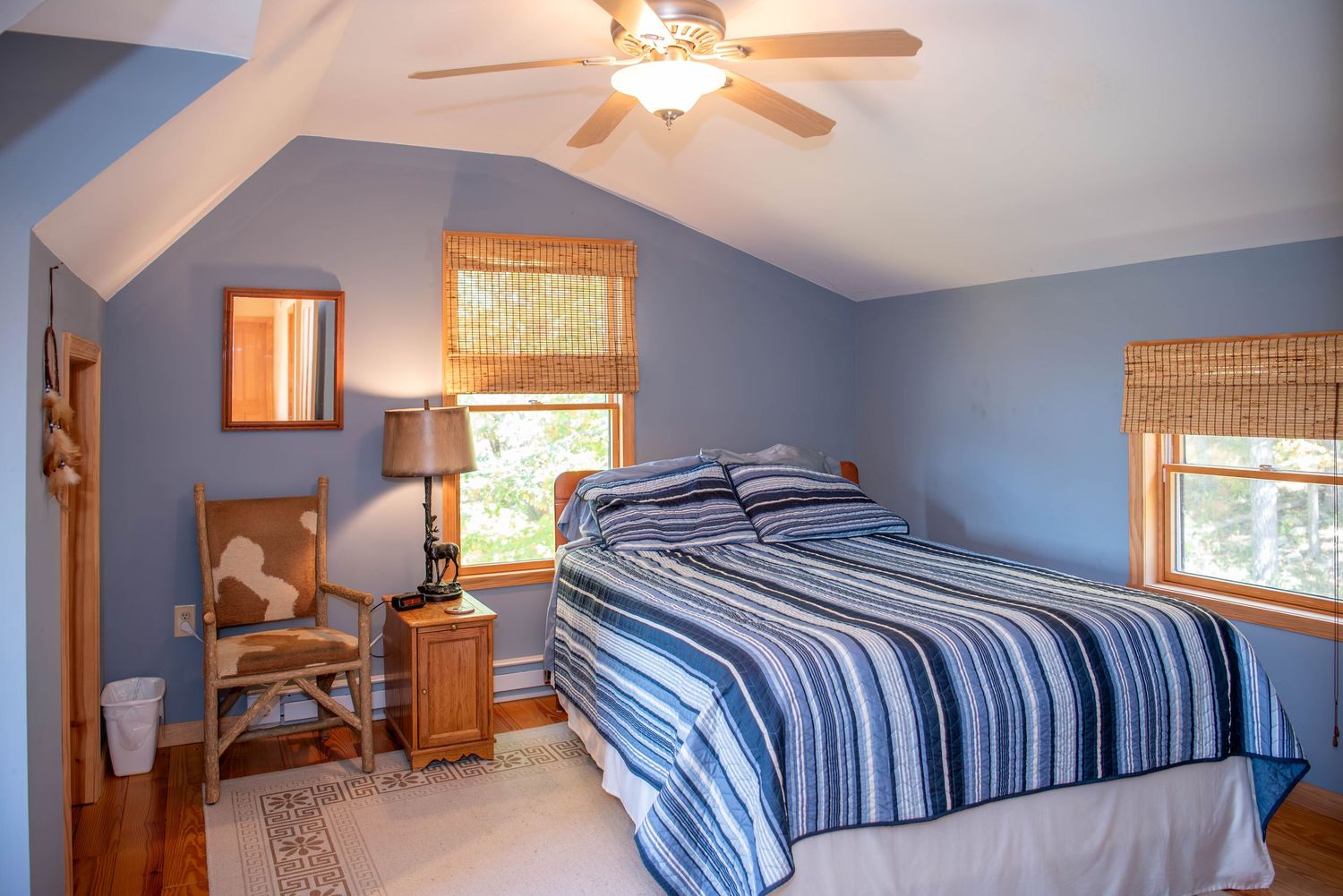 Cozy blue bedroom with vaulted ceiling, twin beds, and natural light streaming through multiple windows.