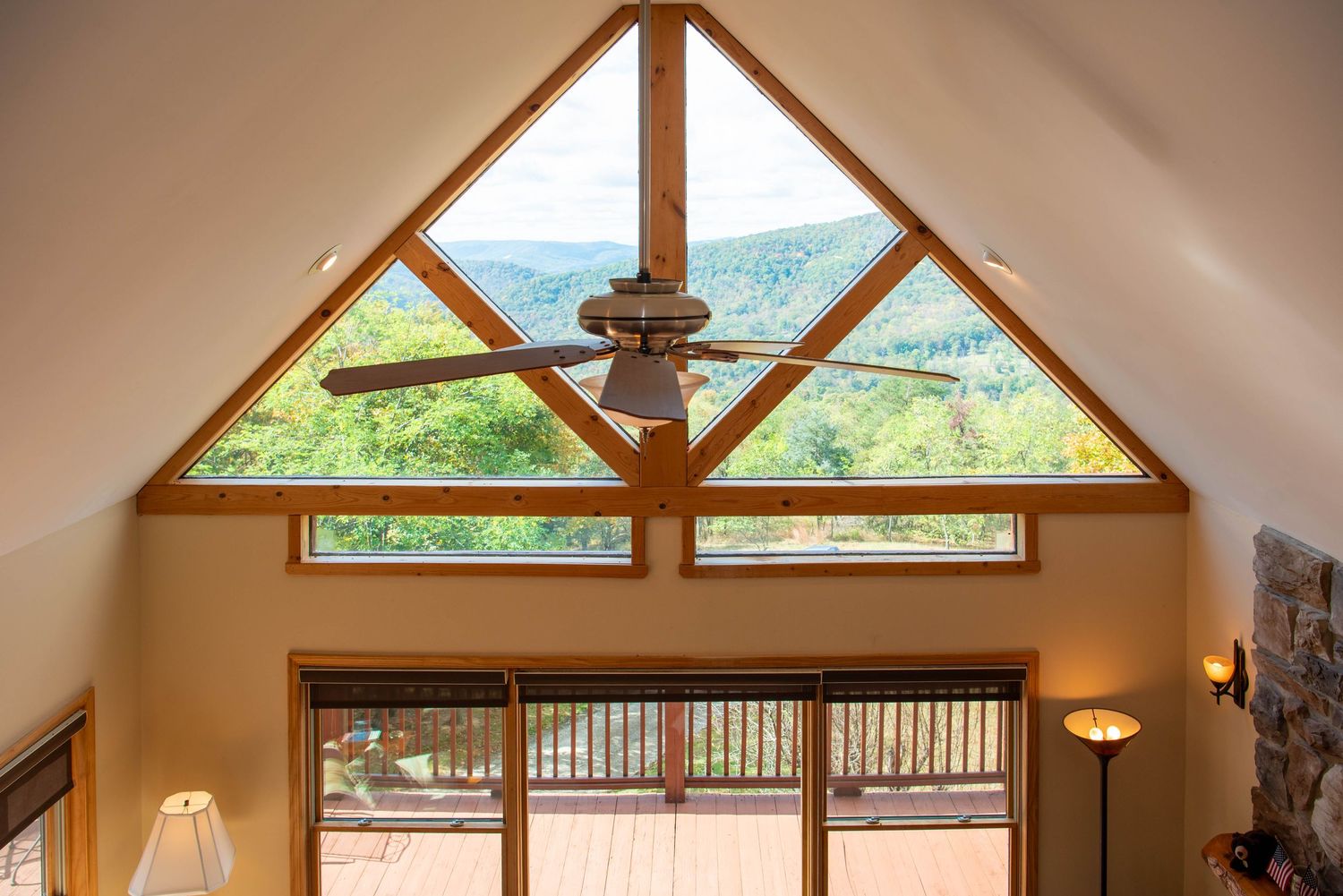 Triangular window design in vaulted ceiling with ceiling fan and mountain views through glass panels.