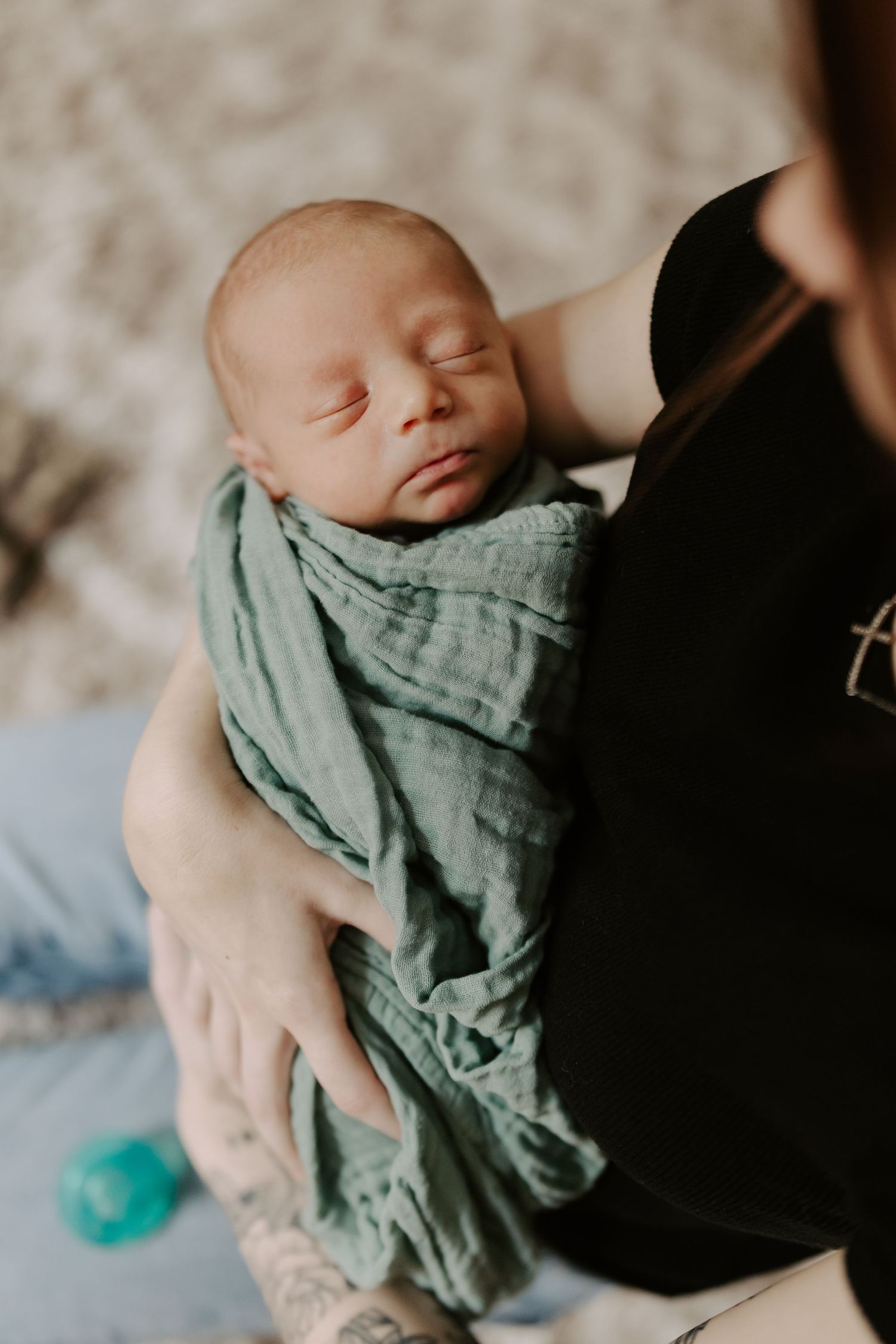 Peaceful sleeping newborn wrapped in sage green swaddle being held.