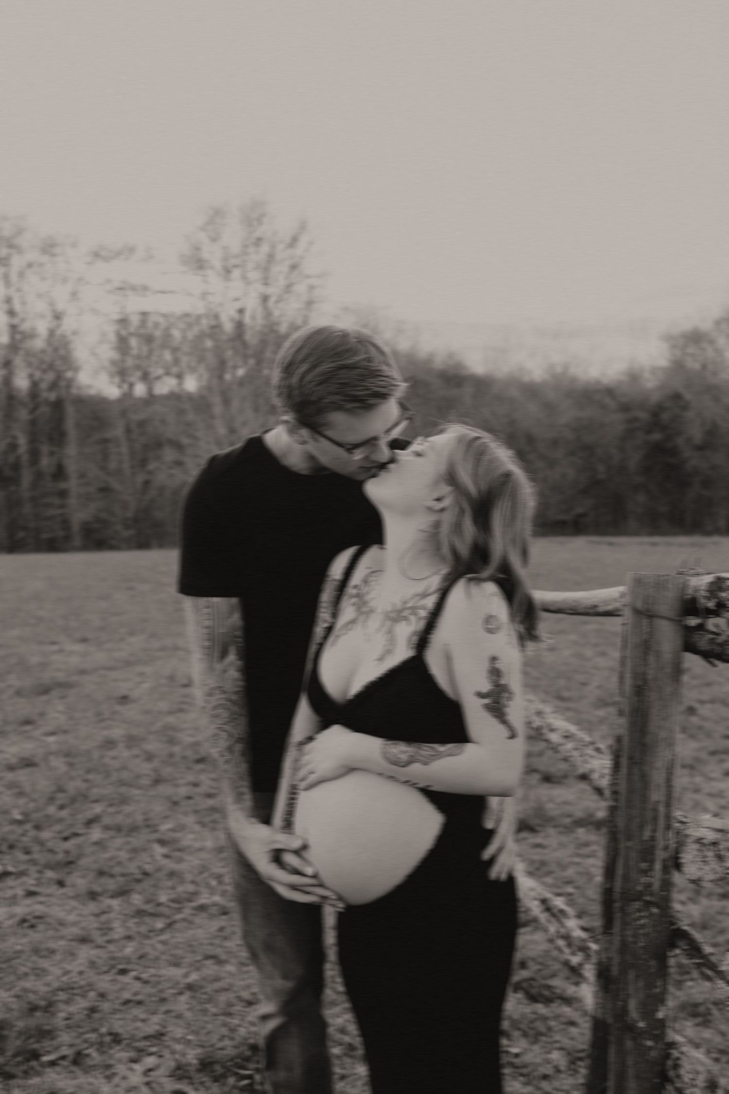 Intimate black and white maternity photo of couple by rustic fence.