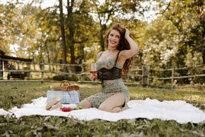 Outdoor autumn picnic setup with wine and snacks on a white blanket near a wooden fence.