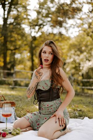 Outdoor picnic scene with floral dress and wine glass against golden autumn foliage.