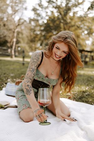 Relaxed outdoor picnic with wine glass on white blanket in park setting.