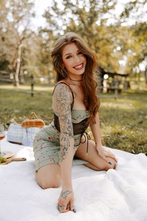 Picnic scene with model wearing mint green dress lounging on white blanket in autumn park setting.