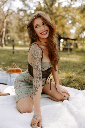 Outdoor portrait featuring tattooed model in mint dress relaxing on white picnic blanket.