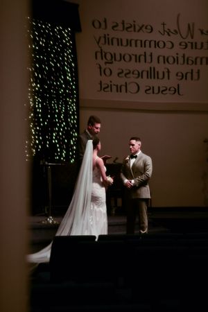 A dramatic wedding scene unfolds in a dimly lit church with string lights creating a romantic atmosphere.