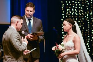 Wedding ceremony moment in front of a blue backdrop with string lights.