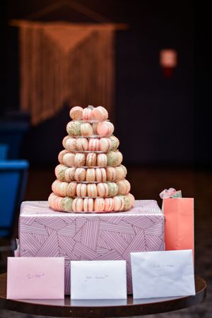 Delicate pink macarons arranged in tiers on a geometric patterned box with coral candles for decoration.