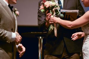 Close-up of wedding bouquet with pink and white flowers being exchanged during ceremony.