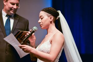 A couple exchanges personal vows during their wedding ceremony against a blue-lit backdrop.